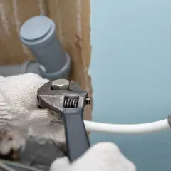 Ręce w rękawiczkach dokręcają kluczem hydrauliczne połączenie, przygotowując instalację, jak zamontować syfon do pralki.