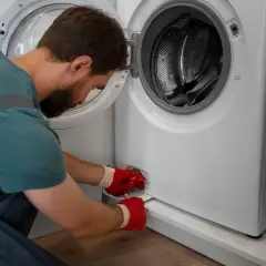 Serwisant w czerwonych rękawicach naprawia pralkę, która wydaje głośne stukanie.