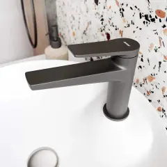Nowoczesna, grafitowa bateria łazienkowa z płaską wylewką, z subtelnym odpryskiem na czarnej baterii, na białej umywalce.