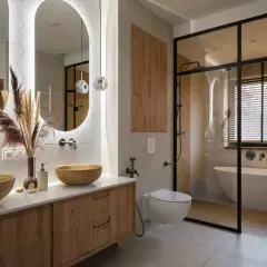 Nowoczesna łazienka z drewnianymi akcentami, dwoma umywalkami i wanną w przeszklonej kabinie. Inspiracja, jak urządzić łazienkę w stylu boho-chic.