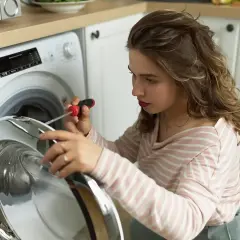 Kobieta naprawia pralkę e10 electrolux, używając śrubokręta.
