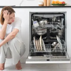 Zmartwiona kobieta siedzi obok otwartej zmywarki Bosch, która nie chce się wyłączyć. W środku brudne naczynia.