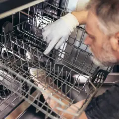 Mężczyzna w rękawiczce sprawdza wnętrze zmywarki Bosch. Może to być kontrola przed uruchomieniem lub po awarii, gdy miga kranik.