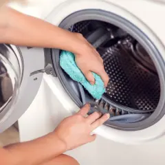 Ręce czyszczą gumową uszczelkę bębna pralki Samsung niebieską ściereczką. Dbałość o czystość pralki to podstawa.