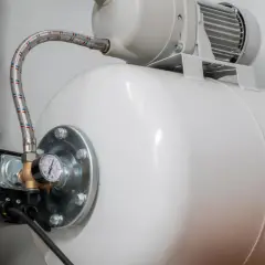 Biały zbiornik hydroforowy z manometrem i wężem. Obok zbiornik IBC. Może to oznaczać, że hydrofor często się włącza.