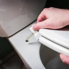 Dłoń przykłada element deski sedesowej do otworu. Dowiedz się, jak zmierzyć deskę sedesową, by dopasować ją idealnie.