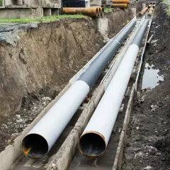 Dwie duże rury ułożone w wykopie. Nie widać, na jakiej głębokości rura z wodą, ale prace budowlane trwają.