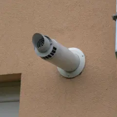 Wyrzut boczny spalin przez ścianę z elewacją, obok metalowy kanał wentylacyjny.