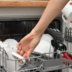 Ręka wkłada kubek do zmywarki, pokazując, jak działa zmywarka. Naczynia czekają na umycie.
