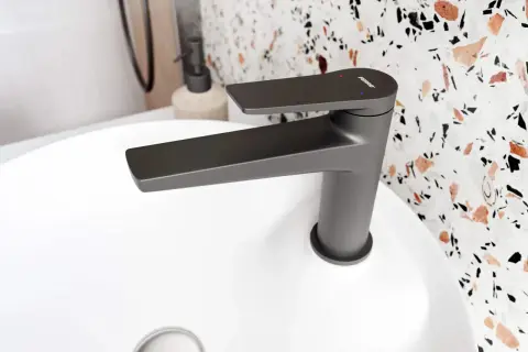 Nowoczesna, grafitowa bateria łazienkowa z płaską wylewką, z subtelnym odpryskiem na czarnej baterii, na białej umywalce.