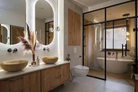 Nowoczesna łazienka z drewnianymi akcentami, dwoma umywalkami i wanną w przeszklonej kabinie. Inspiracja, jak urządzić łazienkę w stylu boho-chic.