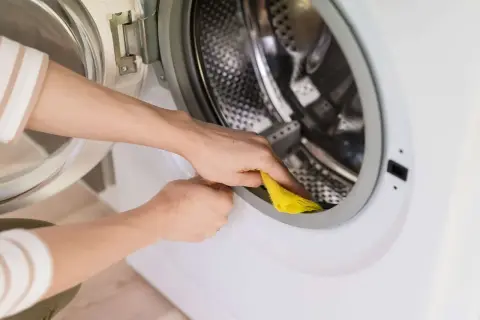 Ręce czyszczą uszczelkę pralki żółtą ściereczką. To część programu czyszczenie bębna, by utrzymać urządzenie w czystości.