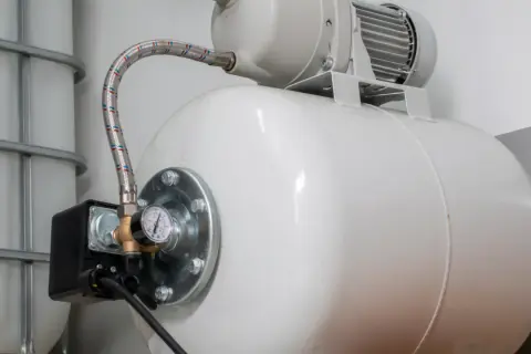 Biały zbiornik hydroforowy z manometrem i wężem. Obok zbiornik IBC. Może to oznaczać, że hydrofor często się włącza.