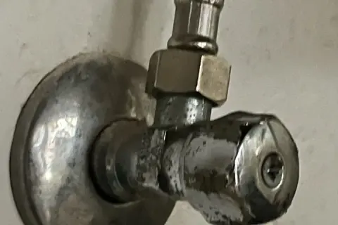 Metalowy zawór przy ścianie. Aby zamknąć wodę, należy go odkręcić w lewo.
