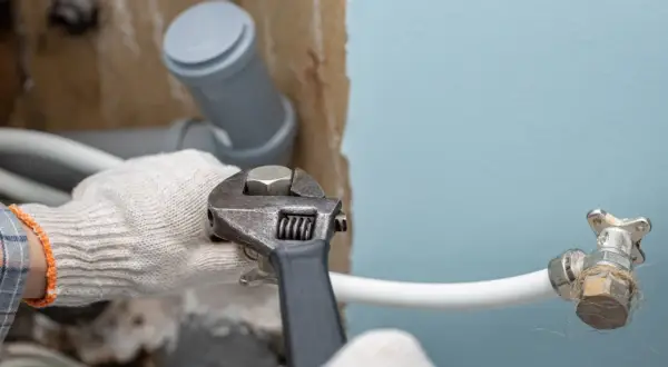 Ręce w rękawiczkach dokręcają kluczem hydrauliczne połączenie, przygotowując instalację, jak zamontować syfon do pralki.