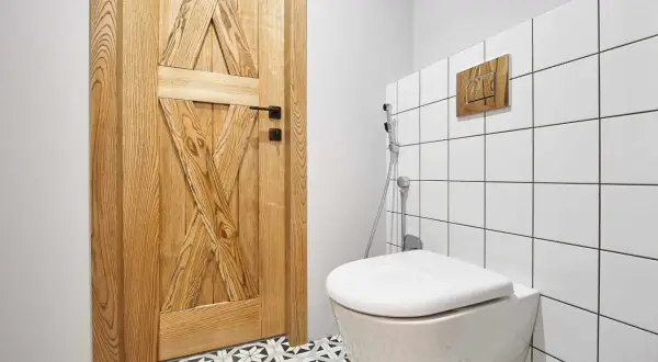 Nowoczesna zabudowa w łazience: drewniane drzwi, białe kafelki i elegancka armatura.