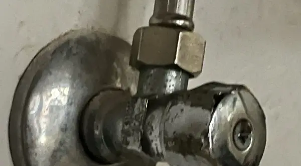 Metalowy zawór przy ścianie. Aby zamknąć wodę, należy go odkręcić w lewo.