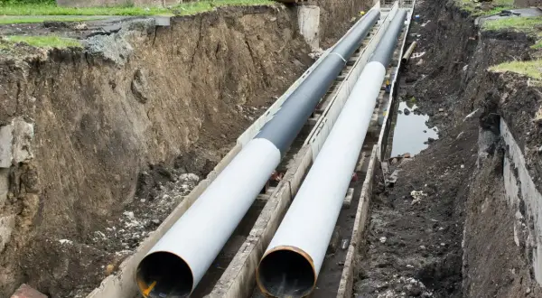 Dwie duże rury ułożone w wykopie. Nie widać, na jakiej głębokości rura z wodą, ale prace budowlane trwają.