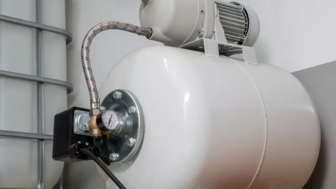 Biały zbiornik hydroforowy z manometrem i wężem. Obok zbiornik IBC. Może to oznaczać, że hydrofor często się włącza.
