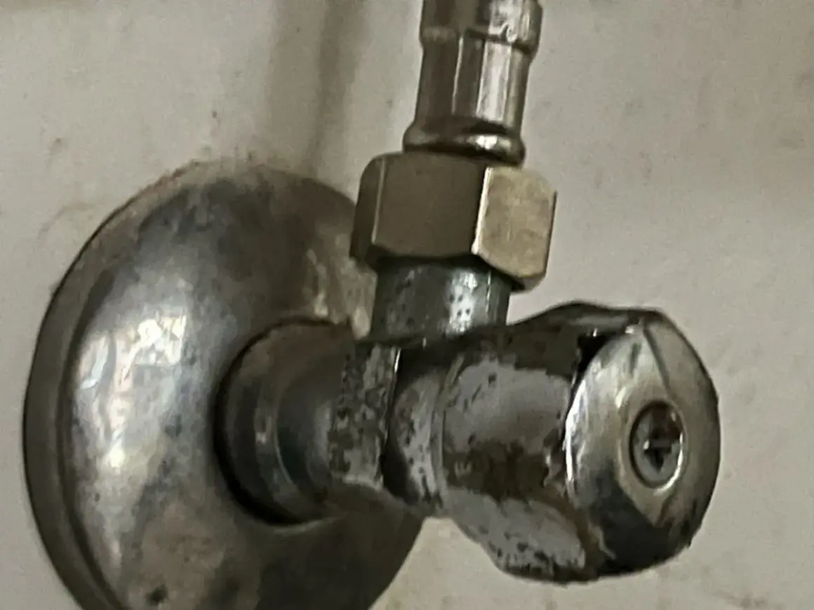 Metalowy zawór przy ścianie. Aby zamknąć wodę, należy go odkręcić w lewo.