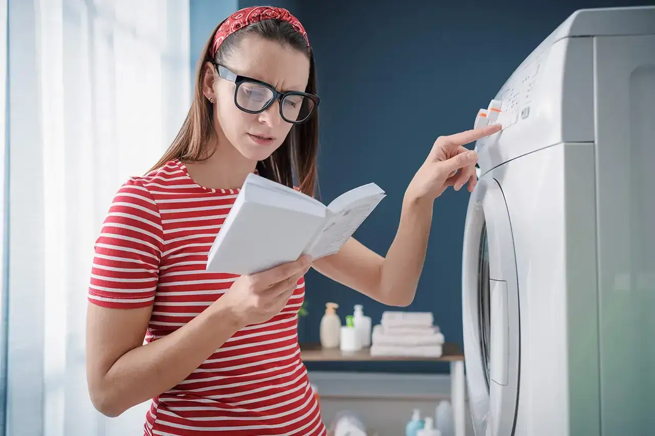 Kobieta z okularami i czerwoną opaską na włosach czyta instrukcję do pralki e10 electrolux, naciskając przycisk.