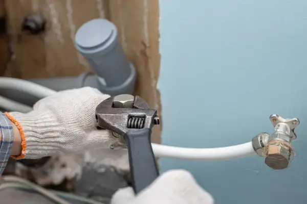 Ręce w rękawiczkach dokręcają kluczem hydrauliczne połączenie, przygotowując instalację, jak zamontować syfon do pralki.