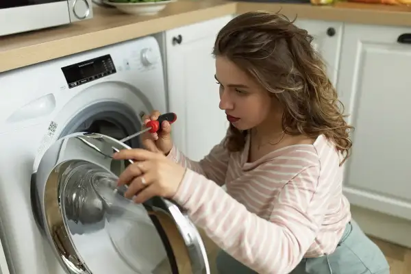 Kobieta naprawia pralkę e10 electrolux, używając śrubokręta.