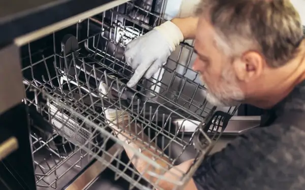 Mężczyzna w rękawiczce sprawdza wnętrze zmywarki Bosch. Może to być kontrola przed uruchomieniem lub po awarii, gdy miga kranik.