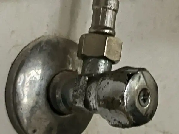 Metalowy zawór przy ścianie. Aby zamknąć wodę, należy go odkręcić w lewo.