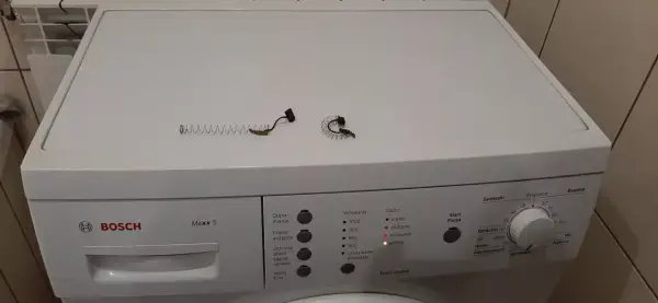 Części do wymiany szczotek w pralce Bosch Maxx 5 leżą na jej obudowie.
